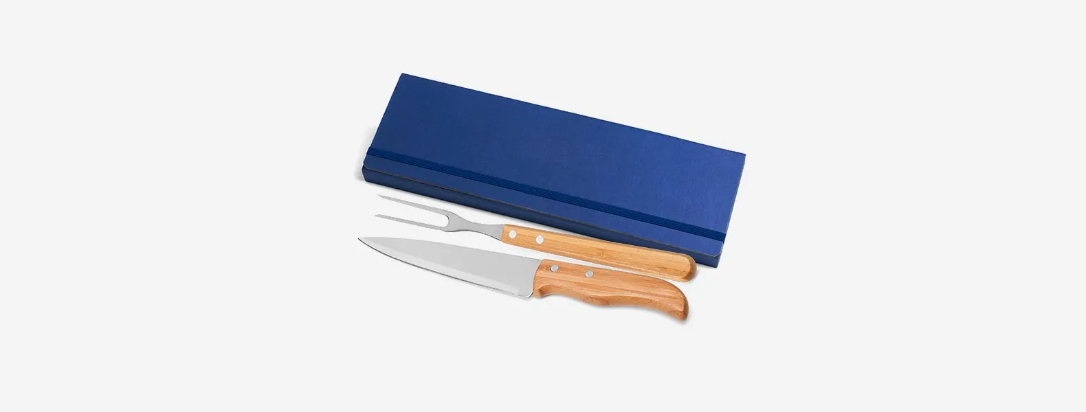 Conjunto composto por uma faca 7” e um garfo trinchante, ambos com cabos em bambu e lâminas em aço Inox com rebites resistentes. Estão organizados em uma pasta azul com elásticos.