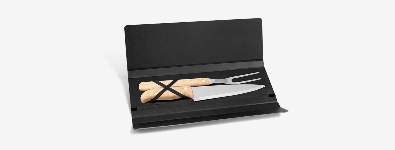 Conjunto composto por uma faca 7” e um garfo trinchante, ambos com cabos em madeira e lâminas em aço Inox. Estão organizados em uma pasta preta com elásticos.