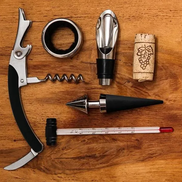 Kit para vinho. Composto por cinco acessórios para vinho em metal e inox, sendo um anel corta-gotas, um funil direcionador com tampa e tampão, ambos com detalhes emborrachados para melhor fixação na garrafa, um termômetro e um abridor saca-rolhas modelo sommelier de alavanca simples com três funções acomodados em um estojo em bambu.